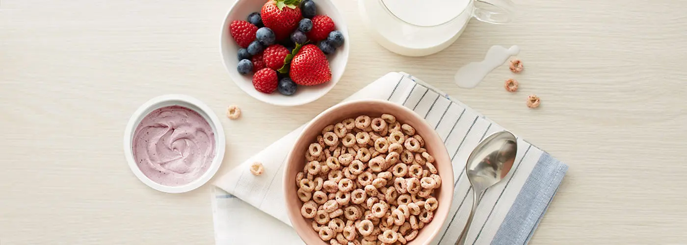 A top view of a table with a bowl of cereal, a cup of yogurt, a bowl of fruit, and a glass of milk