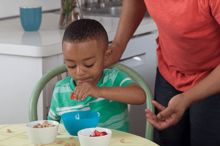 A child eating breakfast at a table with a parent nearby.