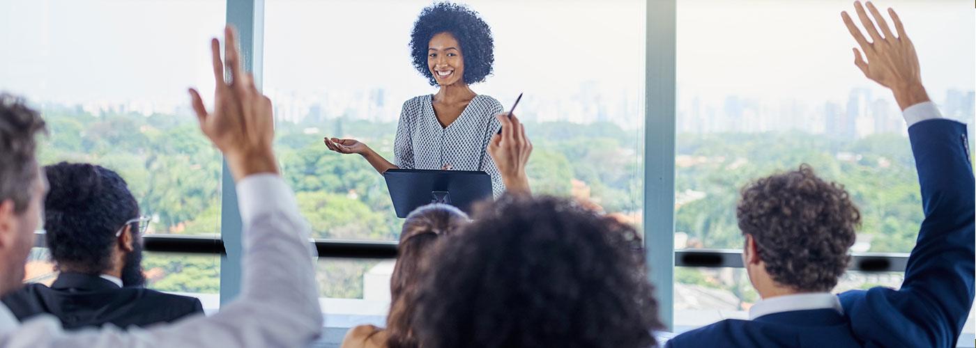 A public speaker smiling and looking at a crowd of business people raising their hands to ask questions