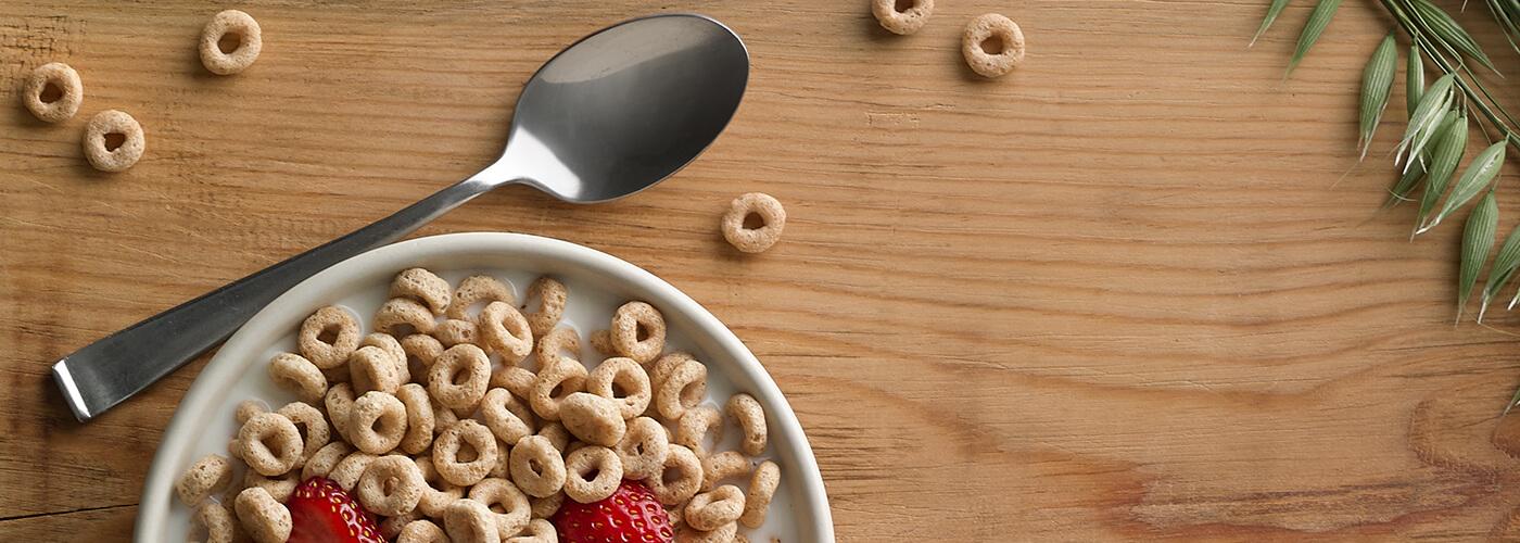 A top view of a table with a bowl of cereal next to a metal spoon.