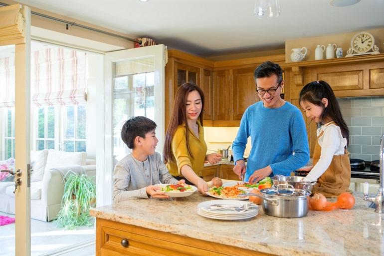 A mum, dad, & two children standing at a kitchen island with plated healthy meals that include many vegetables.