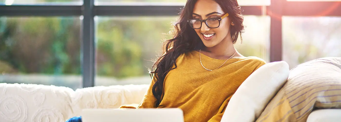 A person wearing glasses is sitting and looking down towards a white laptop.