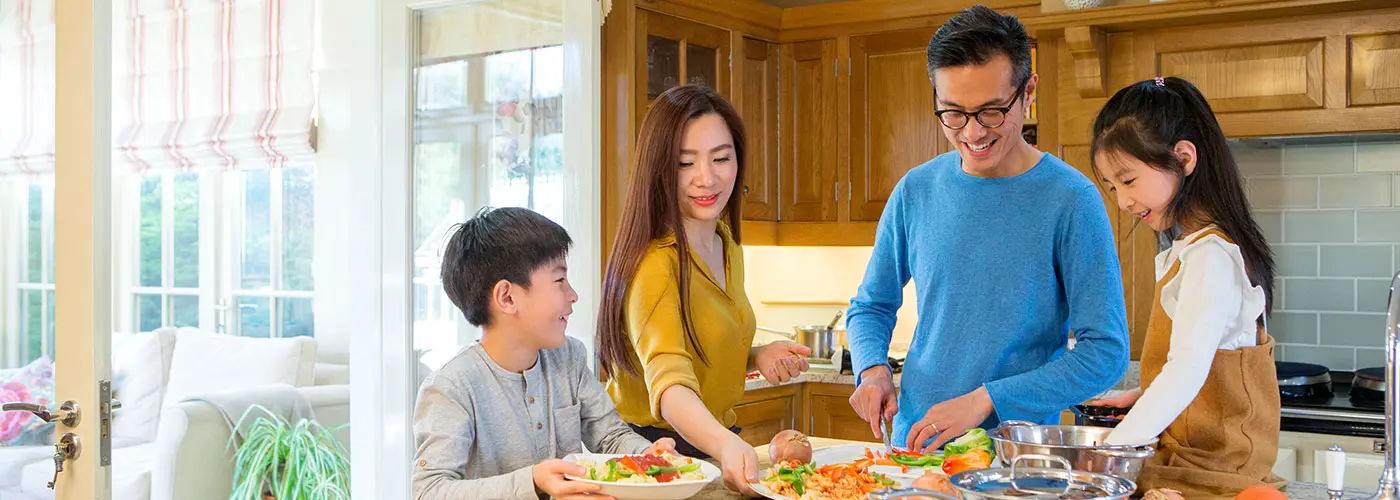 A close up of parents & two children stood at a kitchen island with plated healthy meals that include many vegetables.